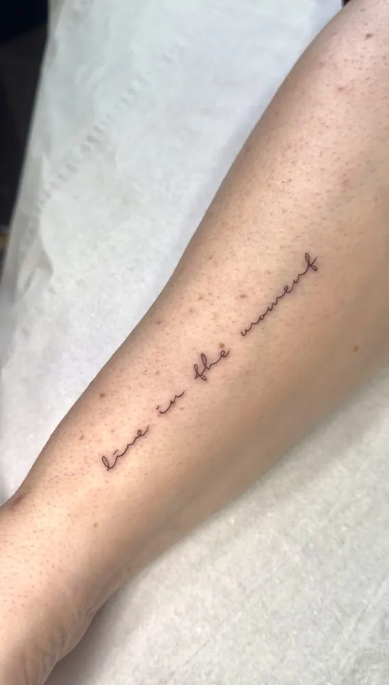 Tatuaje de la frase «live in the moment» en caligrafía